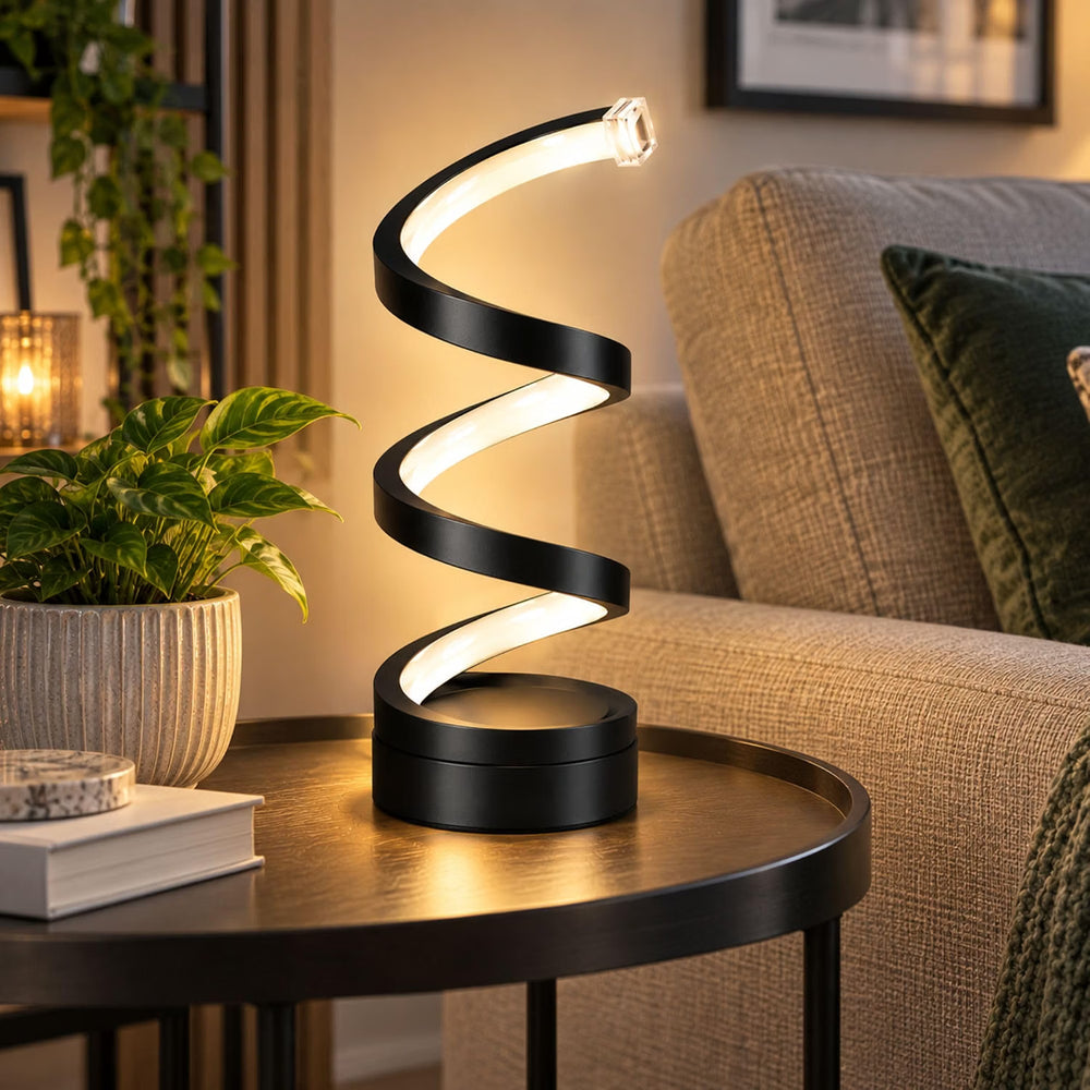 A modern spiral-shaped table lamp with a black frame and glowing white LED light, placed on a round wooden side table in a cozy living room next to a sofa and potted plant.