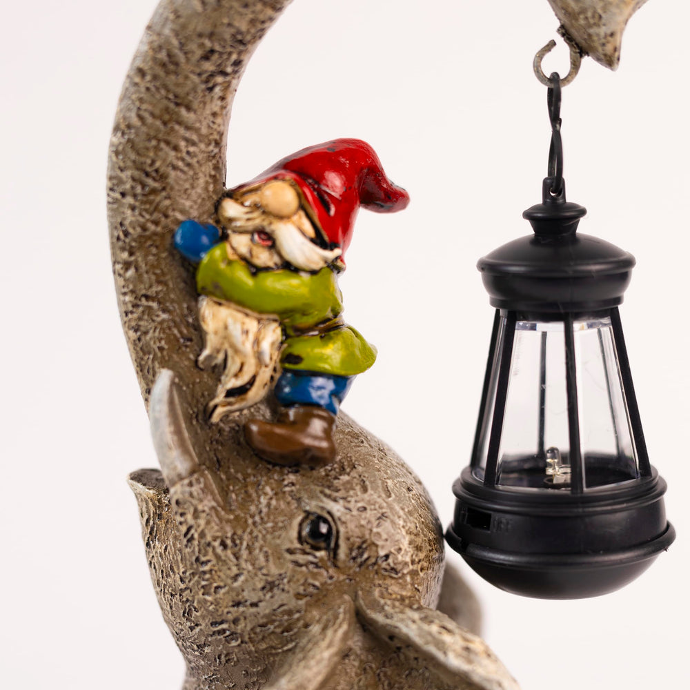 A solar garden ornament featuring a stone elephant sitting on grass with a small figurine of a person on its back holding a lantern, at dusk.