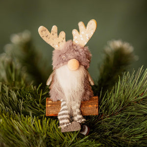Decorative gnome with reindeer antlers sitting on a branch against a green background
