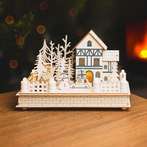 Wooden Christmas village scene with a house, trees, and car on a wooden base.
