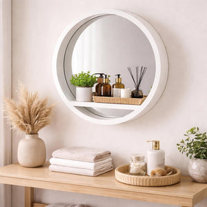 Round mirror on a wall with decorative items on a wooden shelf below.