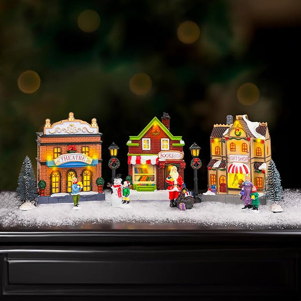 Christmas village scene with miniature buildings and figures on a snowy surface.