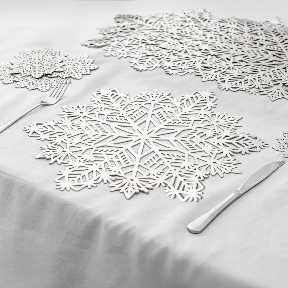 White snowflake-shaped table placemats arranged on a white tablecloth, with a fork and knife placed beside them.