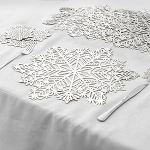White snowflake-shaped table placemats arranged on a white tablecloth, with a fork and knife placed beside them.