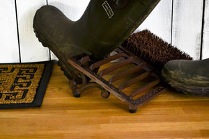 Black rubber boots on a wooden floor with a brush and doormat.