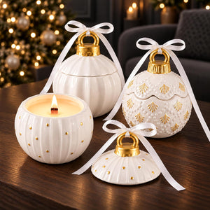 Three white ceramic Christmas ornament-shaped candle holders with gold accents and white ribbon bows, arranged on a dark wooden table with a blurred Christmas tree in the background.