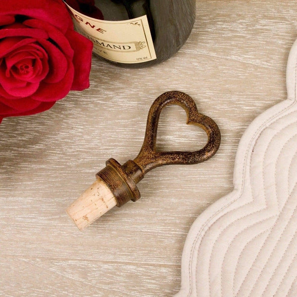 Heart-shaped bottle opener with cork on a wooden surface next to a red rose and wine bottle.