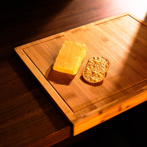 Block of cheese and cracker on a wooden cutting board with warm lighting