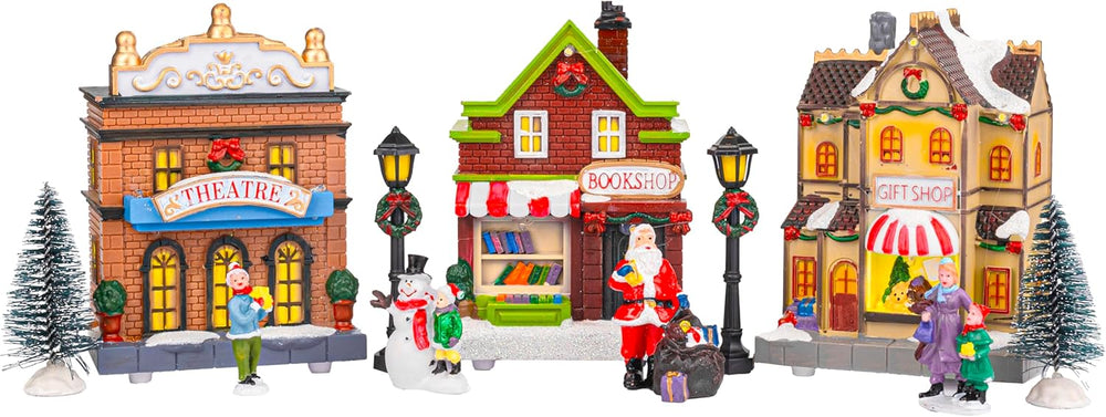 Christmas village scene with miniature buildings and figures on a snowy surface.