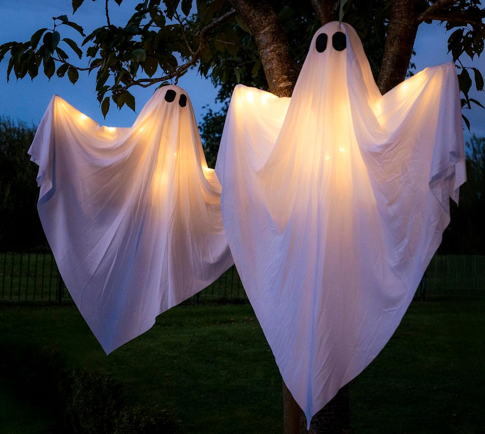 Two illuminated ghost decorations hanging from a tree at night.