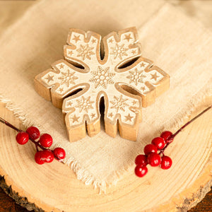 Wooden snowflake ornament with engraved patterns on a wooden surface with red berries.