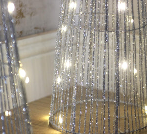 Bottom of pre lit silver sparkle tree in a room setting against a textured wall.