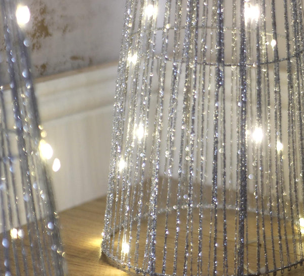 Bottom of pre lit silver sparkle tree in a room setting against a textured wall.
