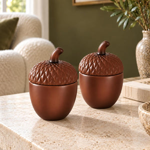 Two brown acorn-shaped decorative jars with matching lids, displayed on a light stone countertop in a cozy kitchen or dining setting.