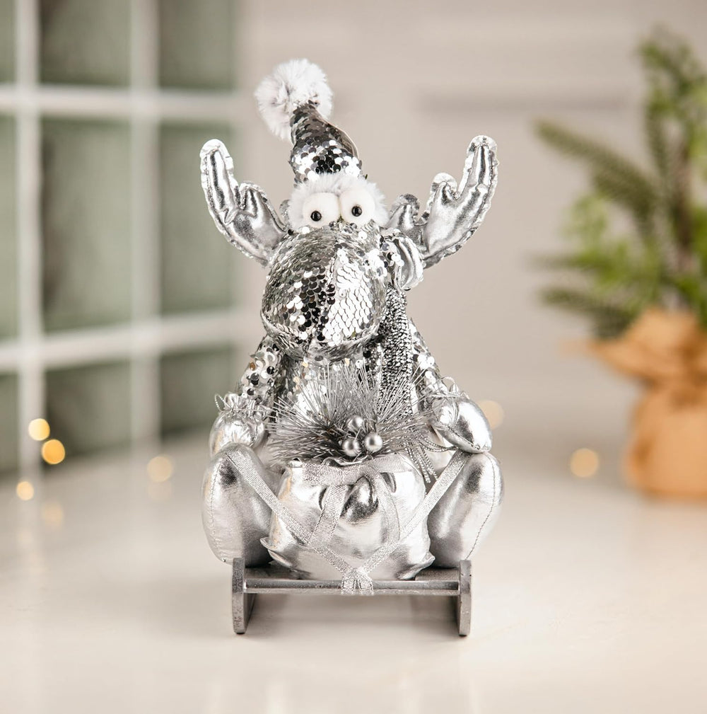 Decorative silver reindeer figure with a small snowman on its back, set against a blurred indoor background.