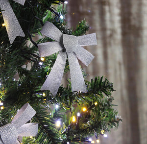 Silver glittery bows on a Christmas tree with blurred background