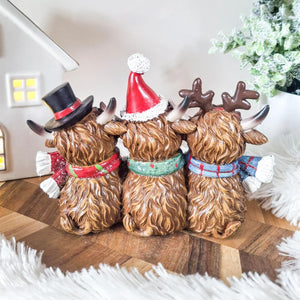 Three decorative figures of dogs wearing festive hats and scarves on a wooden surface.