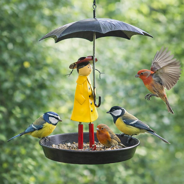 Bird feeder with a person in a yellow raincoat and umbrella, surrounded by birds against a green background.