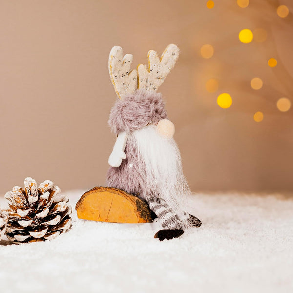 Decorative gnome with antlers on a wooden log, surrounded by pine cones and a blurred light background