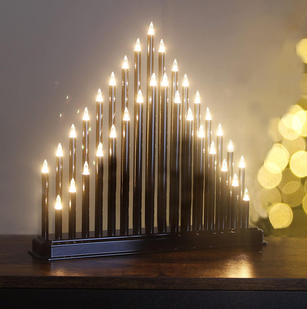 Decorative candle-like structure with lights on a wooden surface, blurred lights in the background
