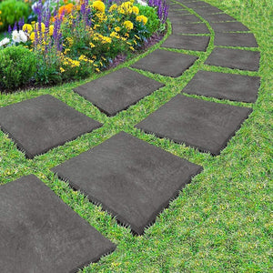 Gray stepping stones arranged in a circular pattern on grass with flowers in the background