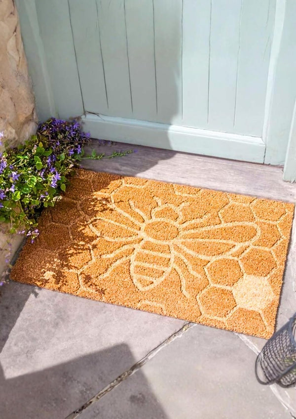 Decorative doormat with floral design on a stone floor in front of a door.