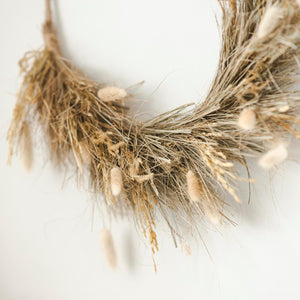 Decorative wreath made of dried grasses and bunny tails on a white background