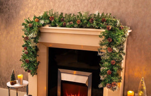 Decorative Christmas garland on a fireplace mantel with candles and small trees.