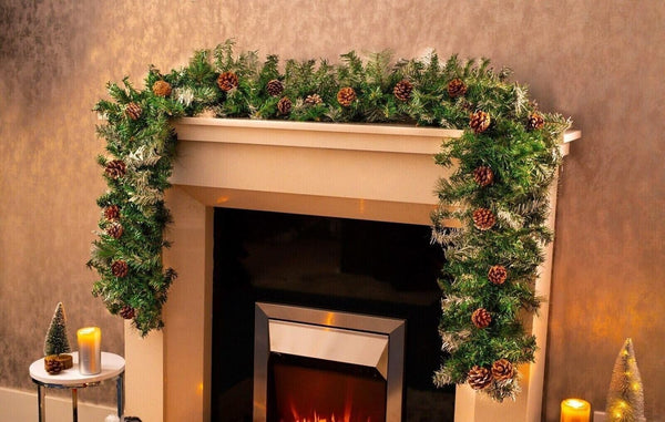 Decorative Christmas garland on a fireplace mantel with candles and small trees.
