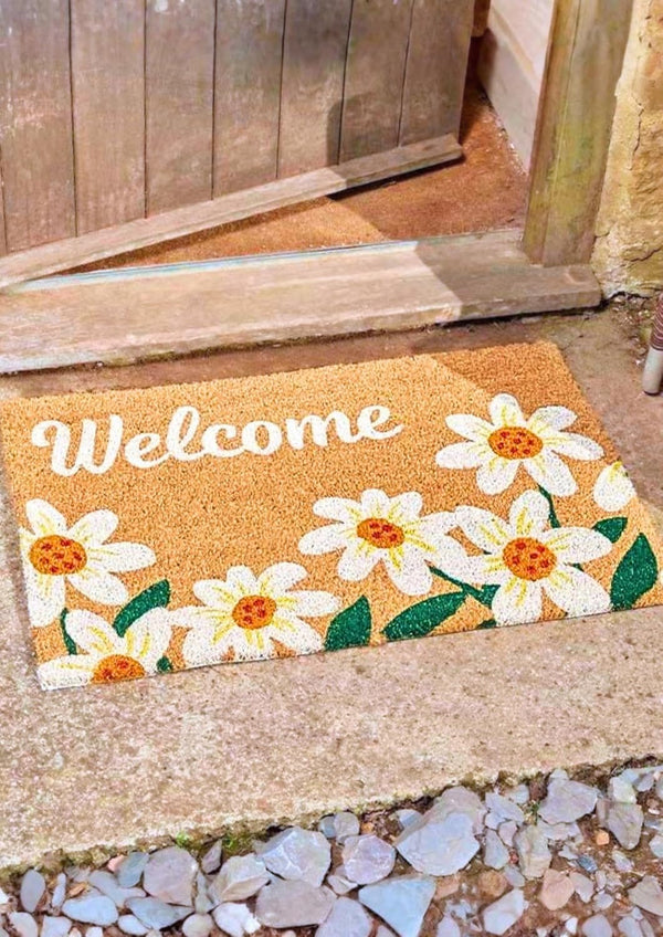 Doormat with floral design and 'Welcome' text on a stone floor.
