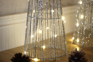 Bottom of pre lit silver sparkle tree in a room setting against a textured wall, with acorns scattered on the floor.