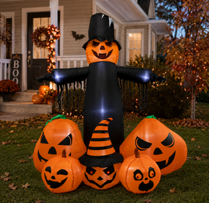 Inflatable Halloween yard decoration set featuring a large black witch-hat scarecrow with glowing blue-white arms, surrounded by five orange jack-o'-lantern pumpkins with carved faces, displayed on a lawn in front of a decorated house at dusk.