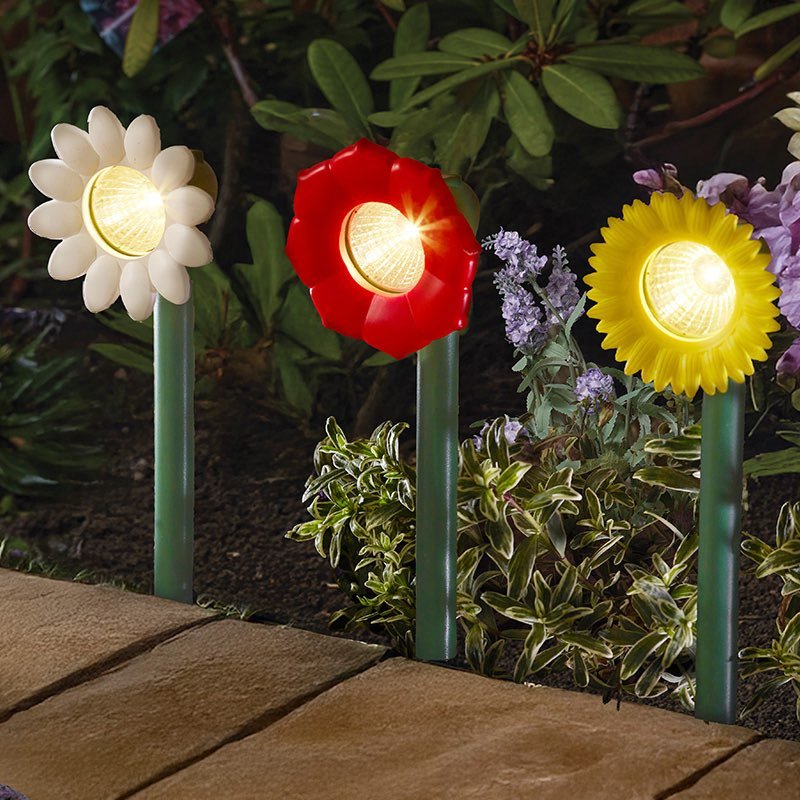 Three colorful flower-shaped solar lights in a garden setting.