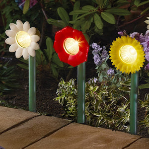 Three colorful flower-shaped solar lights in a garden setting.