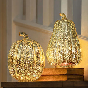 Two decorative glass pumpkins with a sparkling effect on a wooden surface.