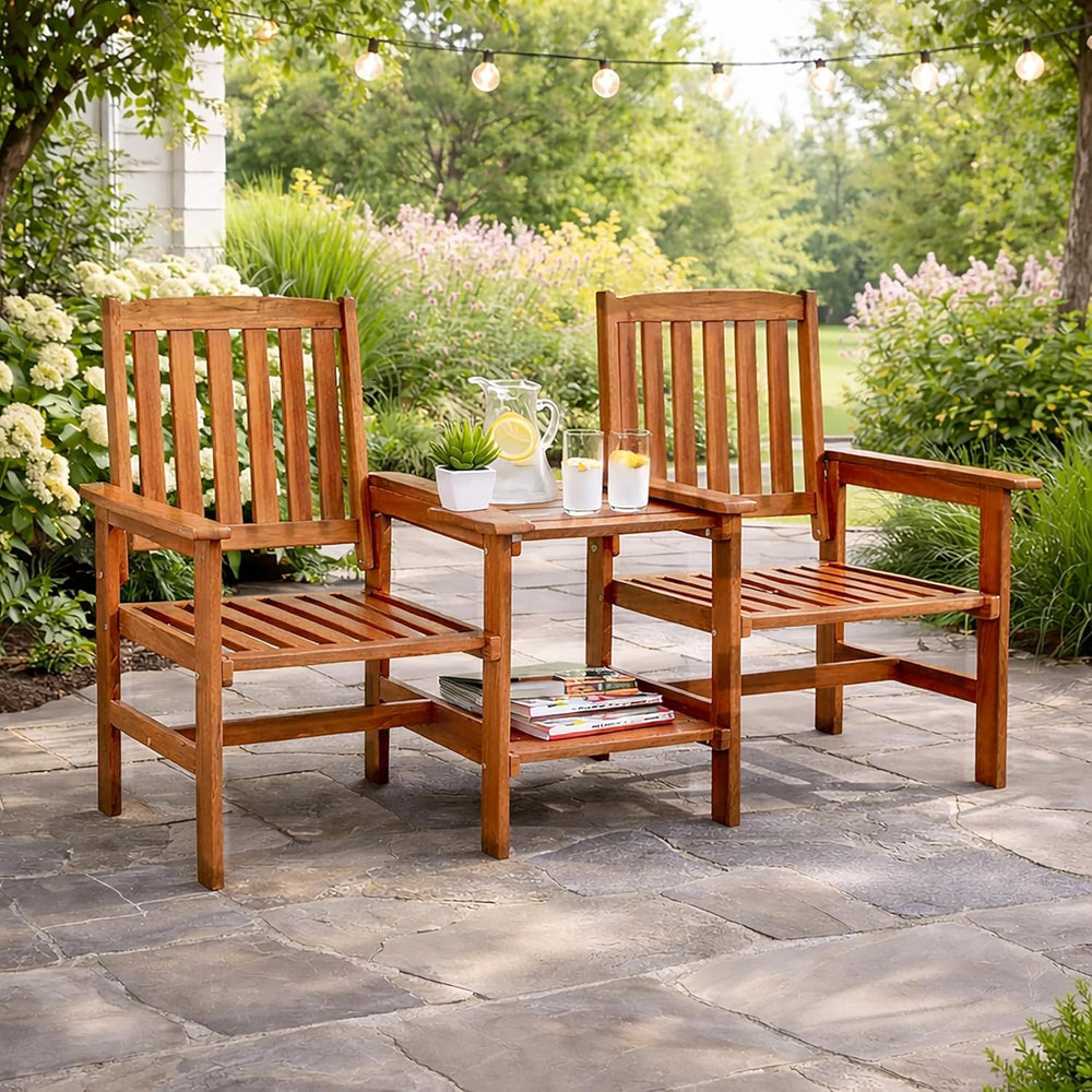 Two wooden chairs with a small table on a stone patio surrounded by greenery.