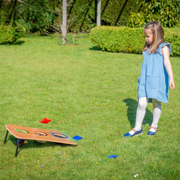 Young girl playing a game of cornhole on a grassy outdoor area