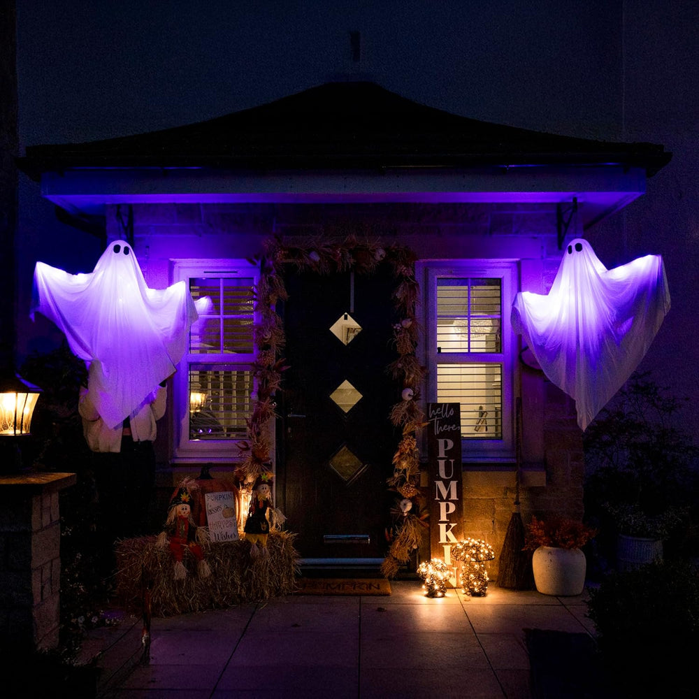 Two illuminated ghost decorations hanging from a tree at night.
