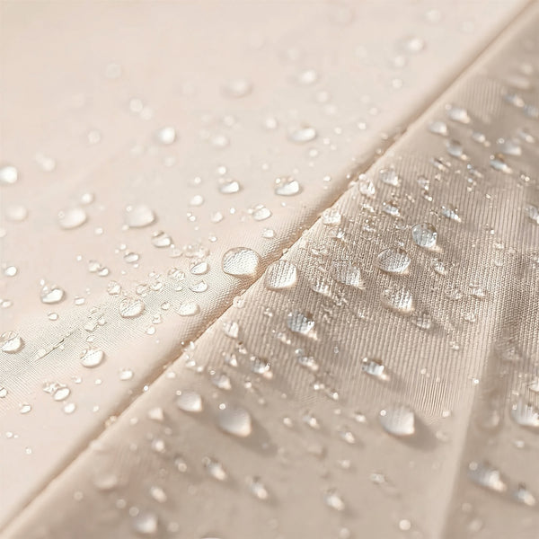 Close-up of a light beige fabric surface with clear water droplets beaded on top and sliding off a slightly textured section, demonstrating a water-repellent finish.