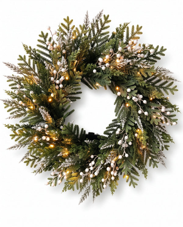 A festive artificial Christmas wreath with green pine and fir branches, white berry accents, and warm white string lights, shown against a plain white background.