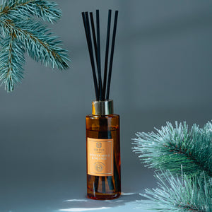 Reed diffuser with decorative sticks on a gray background with pine branches.