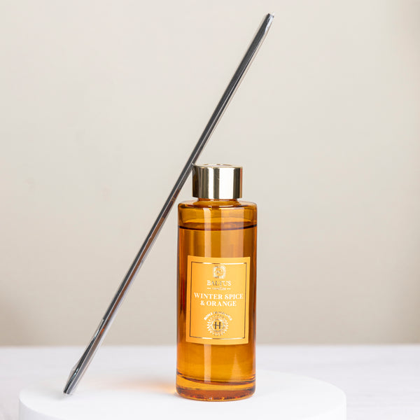 A bottle of 'Winter Spice Romance' diffuser with a metal diffuser stick on a light background