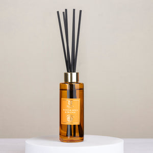 Reed diffuser with black reeds and a gold bottle on a light gray background