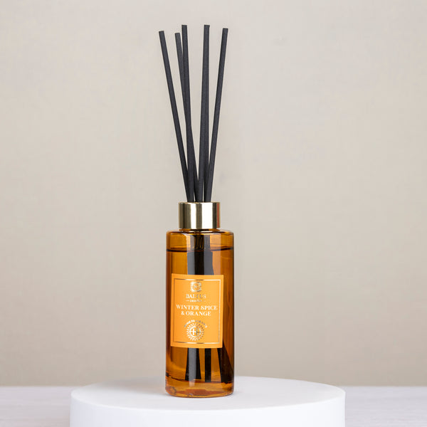 Reed diffuser with black reeds and a gold bottle on a light gray background