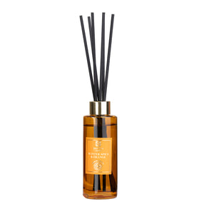 Reed diffuser with black reeds and a gold bottle on a white background