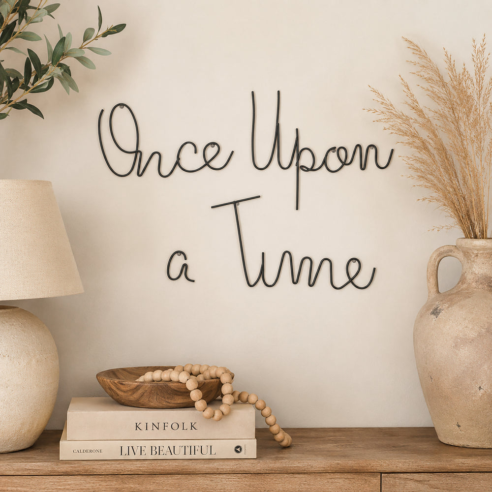 Minimalist black metal "Once Upon a Time" wire wall art mounted on a cream wall above a wooden console with neutral home décor.