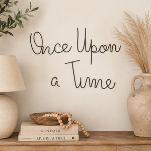 Minimalist black metal "Once Upon a Time" wire wall art mounted on a cream wall above a wooden console with neutral home décor.