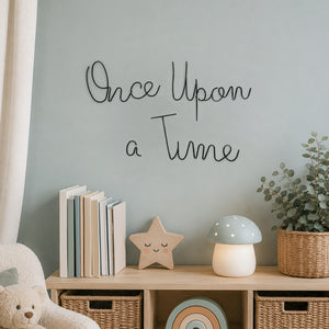 Black metal script wall art reading 'Once Upon a Time' mounted on a light blue wall above a wooden unit styled with a wooden star, mushroom, books, a small basket with a plant in it.
