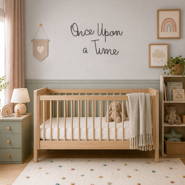 A light natural wood crib in a styled nursery room with a sage green dresser, a white textured blanket, a stuffed bunny, and wall decor including the text 'Once Upon a Time'.