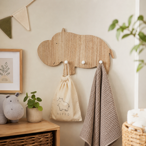 A light natural wood hippo-shaped wall hook rack mounted on a beige wall, holding a cream drawstring bag and a grey textured towel